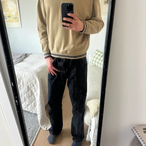 Beige tröja från Weekday - Säljer en beige tröja från Weekday med v-ringad krage och randiga detaljer i blått och beige. Tröjan har långa ärmar och en oversized passform. Perfekt för en avslappnad stil.