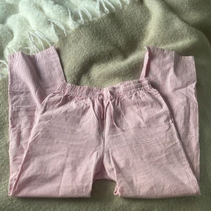 Rosa och vitrandiga byxor - Mysiga rosa och vitrandiga byxor med elastisk midja. Perfekta för en avslappnad dag hemma. Byxorna har en loose passform och är tillverkade i ett mjukt material som känns skönt mot huden.