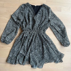 Mönstrad klänning med v-ringning - Snygg klänning med geometriskt mönster. 🖤Den har en v-ringad hals och långa ärmar. Midjan är elastisk för en bekväm passform. Perfekt för en stilfull look och passar till fest, vardags eller andra tillfällen! (Storlek S och okänt märke)
