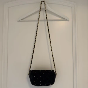 Svart axelväska - Liten axelväska med quiltat mönster och guldfärgade nitar.