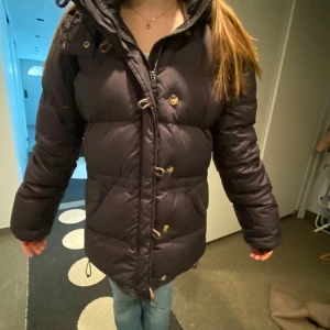 Svart dunjacka från boomerang  - Säljer en svart dunjacka med huva och dragkedja. Jackan har långa ärmar och knappar framtill. Perfekt för kalla dagar med sin pufferdesign som håller värmen. Passar bra för vintern och hösten❤️