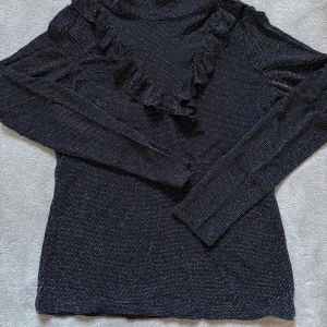 Svart glittrig tröja med volang - Snygg svart tröja med glittrigt mönster och volangdetaljer. 