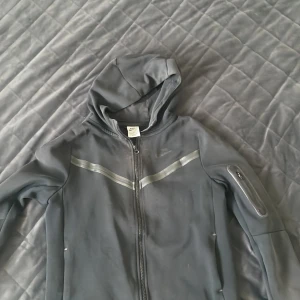 Grå kofta med huva från Nike - Säljer en svart kofta med huva från Nike. Perfekt för en sportig look eller för att hålla sig varm under kyliga dagar. Jackan har en dragkedja framtill och en praktisk ficka med dragkedja på ärmen. Lite sliten men fortfarande i bra skick. Priset kan diskuteras! Koftan är i barnstorlek. 