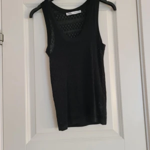 Svart ärmlös topp från Zara - Snygg svart ärmlös topp från Zara med ett diskret hålmönster. Perfekt för lager-på-lager eller att bära som den är. Toppen har en u-ringad design och är tillverkad i ett lätt och bekvämt material.