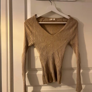 Beige ribbad tröja med v-ringning - Säljer en stilren beige ribbad tröja med v-ringning. Tröjan har långa ärmar och en figurnära passform som passar perfekt för både vardag och fest. Perfekt för höst och vår!
