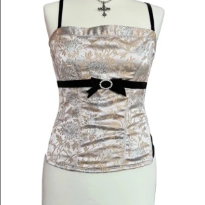 Elegant blommig korsettopp med rosett - Snygg korsettopp med blommigt mönster i guld och silver. Den har smala axelband och en dekorativ svart rosett med en glittrig detalj framtill. Perfekt för en stilfull look. Passar s-m💕
