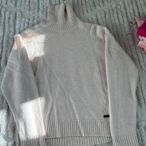 Säljer en stilren beige stickad polotröja från The Kooples. Tröjan har en hög polokrage och ribbstickade detaljer vid ärmslut och nederkant. Perfekt för kyligare dagar och ger en elegant touch till din outfit.