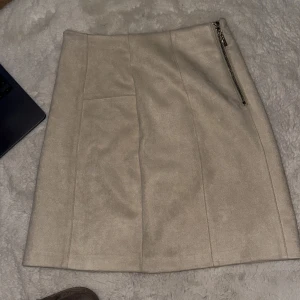 Beige kjol med dragkedja - Snygg beige kjol med dragkedja på sidan. Perfekt för en stilren look. Kjolen har en enkel design och är lätt att matcha med olika toppar.