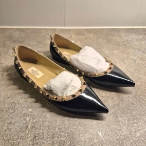 Valentino rockstud  - Snygga svarta ballerinaskor från Valentino med spetsig tå och ikoniska nitar runt kanten. Perfekta för att ge en edgy touch till din outfit. Tillverkade i skinn med en elegant design.
