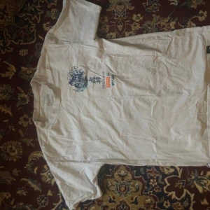 Vit t-shirt med japanskt tryck - Säljer en vit t-shirt med ett coolt japanskt tryck i blått och orange. Motivet föreställer en traditionell japansk figur och en tiger omgiven av vågor. Texten 'Everything you want is on the other side' finns också med. Perfekt för dig som gillar unika och kulturella plagg!