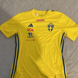 Svenska landslagets fotbollströja Adidas - Gul fotbollströja från Adidas med blå detaljer och svenska landslagets emblem på bröstet. Tröjan har korta ärmar, rund hals och flera sponsorer tryckta på framsidan. Tillverkad i lätt och ventilerande funktionsmaterial för bästa komfort på planen.