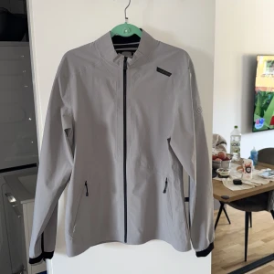 Ljusgrå vindjacka från Sail Racing - 🔔Priset kan diskuteras                             Säljer en stilren ljusgrå vindjacka från Sail Racing. Jackan är tillverkad i polyester med lite stretch, har hel dragkedja framtill, två fickor med dragkedja och diskreta svarta detaljer. Perfekt för dig som gillar sportig och clean look.