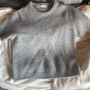 Grå stickad kortärmad tröja från Zara - Mysig grå stickad tröja från Zara med korta ärmar och rund halsringning. Tröjan har en enkel och clean look med ribbade kanter vid hals och nederkant. Köpt för 300kr ish💓
