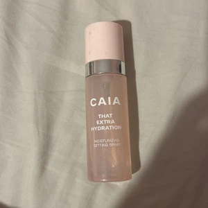 CAIA That Extra Hydration Setting Spray - Återfuktande setting spray från CAIA i en genomskinlig rosa plastflaska med ljusrosa lock och silverdetalj. Perfekt för att ge huden extra fukt och fixera sminket hela dagen. Flaskan rymmer 50 ml och är smidig att ta med i väskan.
