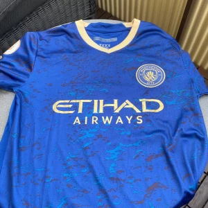 Manchester City Haaland matchtröja blå S - Blå Manchester City fotbollströja med Haaland 9 på ryggen. Guldiga detaljer och klubbmärke på bröstet, samt Etihad Airways-tryck framtill. Kortärmad modell i lätt funktionsmaterial, perfekt för match eller träning.