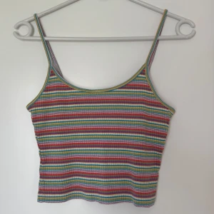 Randigt linn i regnbågsfärger - Färgglad ribbad linnetopp med smala axelband och horisontella ränder i rött, blått, gult, grönt, lila och vitt. Perfekt för dig som gillar retro. 