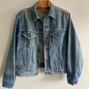 Levi's klassisk blå jeansjacka - Klassisk blå jeansjacka från Levi's med snygga bröstfickor, knappar framtill och coola sömdetaljer. Jackan har en tidlös passform och är tillverkad i slitstarkt denim. Perfekt att slänga över en hoodie eller t-shirt för en avslappnad look. Storlek 46R. Förmodligen en dam med tanke på hur baksidan ser ut. Köpt i en vintage militär butik i Thailand. 