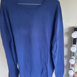 Blå stickad tröja Tiger of Sweden - En stilren blå stickad tröja från Tiger of Sweden i storlek L. Tröjan har rund halsringning och långa ärmar, perfekt för lager-på-lager. Enkel design som funkar till många olika looks.