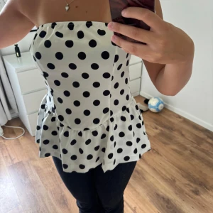 Prickig vit tubtopp med volang - Säljer en söt vit tubtopp med svarta prickar och volang nertill.
