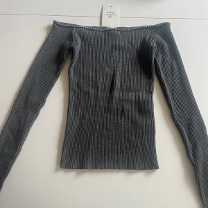 Grå ribbad offshoulder topp H&M S - Snygg grå ribbad offshoulder topp från H&M med långa ärmar och silverfärgade pärldetaljer längs kanten. Toppen är tight och har en stilren, minimalistisk look som passar perfekt till jeans eller kjol.
