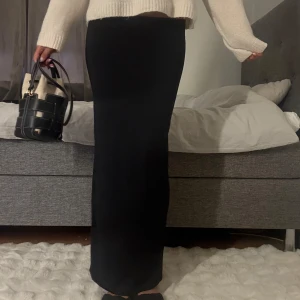 Svart långkjol i stretchigt material - En svart långkjol med rak passform som sitter snyggt och följer kroppen. Kjolen är enkel och stilren, perfekt att matcha med stickad tröja eller crop top. Materialet känns mjukt och stretchigt för extra komfort.