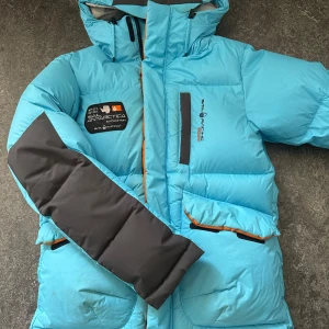 Blå dunjacka Sail Racing  - Säljer denna feta dunjackan från sail racing i en unik colourway som är svår att få tag på. Detta ör en ganska gammal modell på jackan och är ganska använd, därav priset. Den har svarta detaljer på ärmarna och är riktigt fin. Den negativa sidan med den är att den har en stor fläck på luvan men det är det ända. För mer bilder eller information, skriv gärna. Priset kan diskuteras