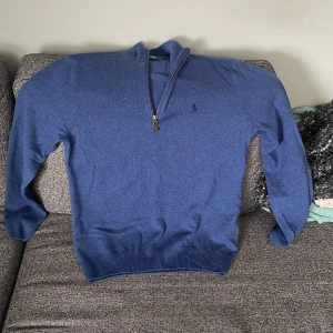 Blå halvzip tröja från Ralph Lauren - Snygg blå långärmad tröja från Ralph Lauren med halv dragkedja och klassisk broderad logga på bröstet. Tröjan är i mjuk bomull och har ribbade muddar vid ärmslut och nederkant. Perfekt för lager-på-lager och chill stil.