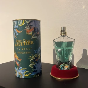 Jean Paul Gaultier Le Beau Paradise Garden 75 ml  - Unik parfym i form av en manlig torso med turkos vätska. Flaskan står på en röd sammetsbas med broderad detalj. Kommer i en grön, blommig och exotiskt dekorerad förpackning med guldtext. Perfekt för dig som gillar snygg design och tropiska vibbar.