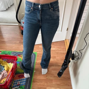 Blå bootcut jeans - Snygga blå jeans med bootcut passform. Klassisk femficksmodell med dragkedja och knapp framtill. Jeansen har en lätt tvättad look och sitter tajt över låren men släpper ut vid vaden. Perfekta för en trendig och avslappnad stil.