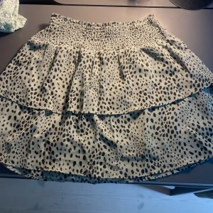 Beige kortkjol med leopardmönster - Supersöt kortkjol i beige med svart leopardmönster och volanger.