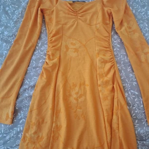 Orange blommig långärmad klänning Gina Tricot - Supersöt orange långärmad klänning från Gina Tricot i storlek XS. Klänningen har blommigt mönster, markerad midja och lätt rynk vid bysten. Mjuk och stretchig bomullsblandning, perfekt för vår och sommar. Snygg passform och skön att bära!