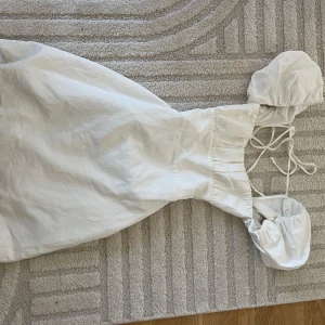 Vit kortklänning med puffärmar - Superfin vit kortklänning med puffiga kortärmar och snygga snörningsdetaljer i ryggen. Klänningen har en söt, romantisk vibe och är gjord i ett lätt bomullstyg som känns luftigt och fräscht. Perfekt för varma dagar när du vill känna dig extra söt.