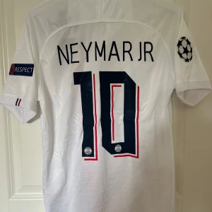 PSG Neymar Jr 19/20 - Säljer en vit PSG fotbollströja med Neymar Jr och nummer 10 på ryggen. Tröjan har även Champions League patches på ärmarna, röd och blå rand på framsidan samt klubbmärke. Fotbolmströjan är också helt oanvänd