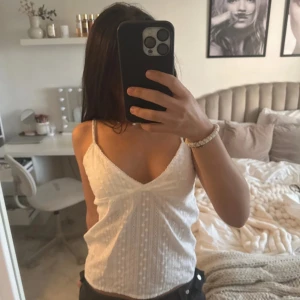 Vit broderad linnetopp med smala band - Superfin vit linnetopp från brandy melville med smala axelband och v-ringning. Toppen har broderade detaljer och diskret prickigt mönster i tyget. Perfekt till jeans eller kjol för en fräsch sommarlook.