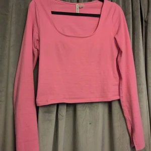 Rosa croppad topp från H&M Divided - Säljer en rosa långärmad croppad topp från H&M Divided. Toppen har en djup, rundad urringning och är tillverkad i mjuk bomull. Passar även Xs eller M beroende på hur man vill att den ska sitta🫶🏻