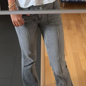 Grå bootcut jeans med sömdetaljer - Snygga grå jeans med markerade sömmar längs benen och bootcut-modell. Byxorna har framfickor med tydliga stickningar och dubbla knappar i midjan. Perfekta för en avslappnad men trendig look.