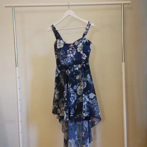 Blommig asymmetrisk klänning Boohoo - Supersnygg marinblå klänning från Boohoo med blommigt mönster och asymmetrisk fåll. Klänningen har breda axelband och är ärmlös, perfekt för sommarens alla tillfällen. Lätt och luftig känsla tack vare det tunna materialet.