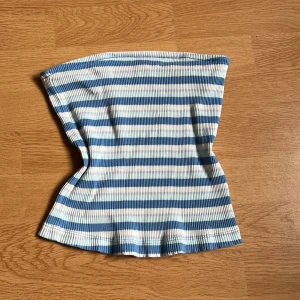 Randig bandeau tubtopp köpt från Nelly - Superfin bandeau tubtopp från Nelly i ribbat material. Toppen har blå, ljusblå och vita ränder och är perfekt för varma dagar. Sitter tight och ärmlös för en clean och trendig look.