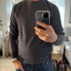 Mörkgrå sweatshirt från Peak Performance - Snygg mörkgrå sweatshirt från Peak Performance med diskret logga på bröstet. Tröjan har rund halsringning, långa ärmar och ribbade muddar vid ärmslut och nederkant. Perfekt för en chill och stilren look.