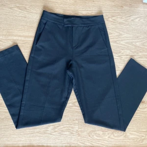 Svarta kostymbyxor från Gina Tricot storlek XS - Svarta kostymbyxor från Gina Tricot i klassisk rak modell. Byxorna har hög midja, diskreta fickor fram och en fuskficka bak. Stängs med dragkedja, hake och knapp. Snygga till skjorta eller stickad tröja.