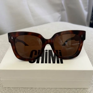 Bruna solglasögon från Chimi - Snygga solglasögon från Chimi med brunmelerat sköldpaddsmönster och bred båge i klassisk cat eye-form. Glasen är bruna och bågarna är tillverkade i acetat för en cool och modern look. Perfekta för att lyfta vilken outfit som helst.