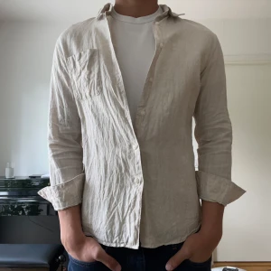 Beige linneskjorta från Uniqlo M - Snygg beige skjorta från Uniqlo i luftig linne, perfekt för varmare dagar. Modellen är 184. Nypris 599kr.