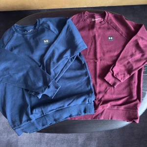Under Armour crewneck i blått & vinrött - Två crewneck-tröjor från Under Armour, en i marinblått och en i vinrött. Klassisk passform med rund hals, långa ärmar och diskret logga på bröstet. Mjukt bomullsmaterial som är skönt mot huden och passar perfekt till jeans eller joggers. 240kr för båda