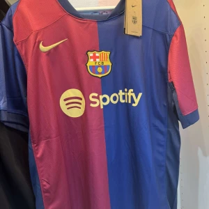 FC Barcelona matchtröja Nike blå/vinröd - Säljer en officiell FC Barcelona matchtröja från Nike med klassisk blå och vinröd färgdelning. Tröjan har klubbmärke, Nike-logga och sponsorer som Spotify och Ambilight tv tryckta på framsidan. Tillverkad i lätt och ventilerande material, perfekt för fotboll eller supporterliv.
