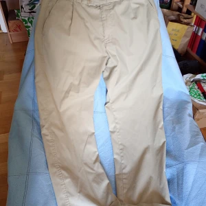 Beiga chinos från Number One KappAhl D104 - Snygga beiga chinos från Number One by KappAhl. Klassisk rak passform med normal midja och diskreta fickor fram. Tillverkade i mjuk bomull som känns skön hela dagen. Perfekta för en clean och stilren look. D104.