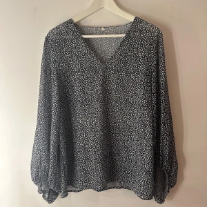 Prickig blus  - En fin prickig blus i vit och blå i storlek L. Något genomskinlig. Blusen är i fint skick men har lite små slitna sömmar intill men den är hel och ren! Tror den är köpt utomlands