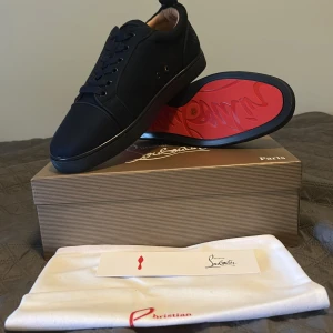 Svarta sneakers från Christian Louboutin - Stilrena svarta sneakers från Christian Louboutin med ikonisk röd sula och diskret logga på insidan. Skorna har rund tå, snörning och är tillverkade i lyxigt skinn med en matt finish. Perfekta för dig som vill ha en exklusiv och clean look. Pris kan diskuteras vid snabb affär 