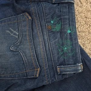 Blå jeans med broderade detaljer - Jättesnygga mid/low waist bootcut jeans med lite slitet jeanstyg, coola fickor och broderade blommor! Midjemåttet är 36 och innerbenslängden är 85 så de passar super för mig som är lite längre!!💓💓