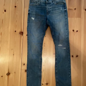 Jack & Jones Slim/Glenn - Snygga blå slim fit jeans från Jack & Jones, modell Slim/Glenn. Jeansen har klassisk femficksdesign, slitna detaljer och normal midja. Tillverkade i stretchig bomullsdenim för en bekväm passform. Perfekta till sneakers och hoodie. Hör gärna av er vid frågor.