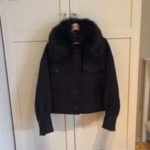 Svart ulljacka med päls från Meotine - Jacka från Meotine i ull med stor äkta päls krage i räv. Storlek S/M. Modellen är croppad med raka ärmar och knappar framtill samt två bröstfickor. Saknar en knapp i mitten, går dock lätt att köpa till. Ursprungligt pris 3000 🖤